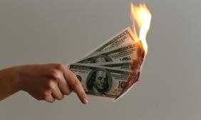 A hand holds US hundred dollar bills that are burning