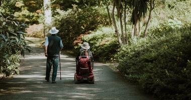 Person with disability riding chair down nature path with friend