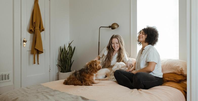 Two women sitting on a bed with a dog. They are having a conversation.