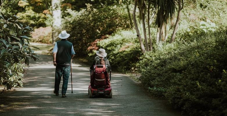 Person with disability riding chair down nature path with friend